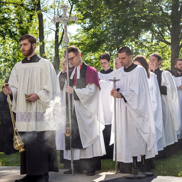 Students in liturgical dress process outdoors at Nashotah House Theological Seminary in Wisconsin led by a thurifer and a crucifer.